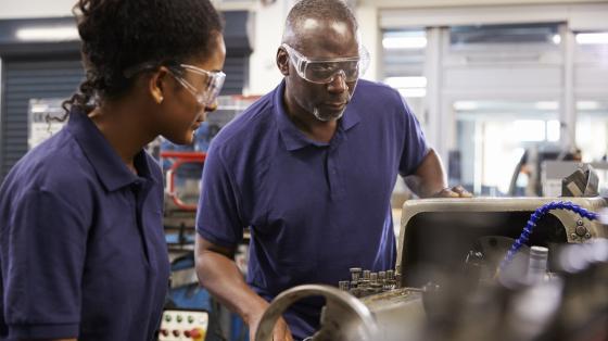 Older African American male mechanic training African American female mechanic in an automotive shop