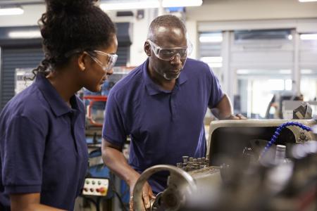 Older African American male mechanic training African American female mechanic in an automotive shop